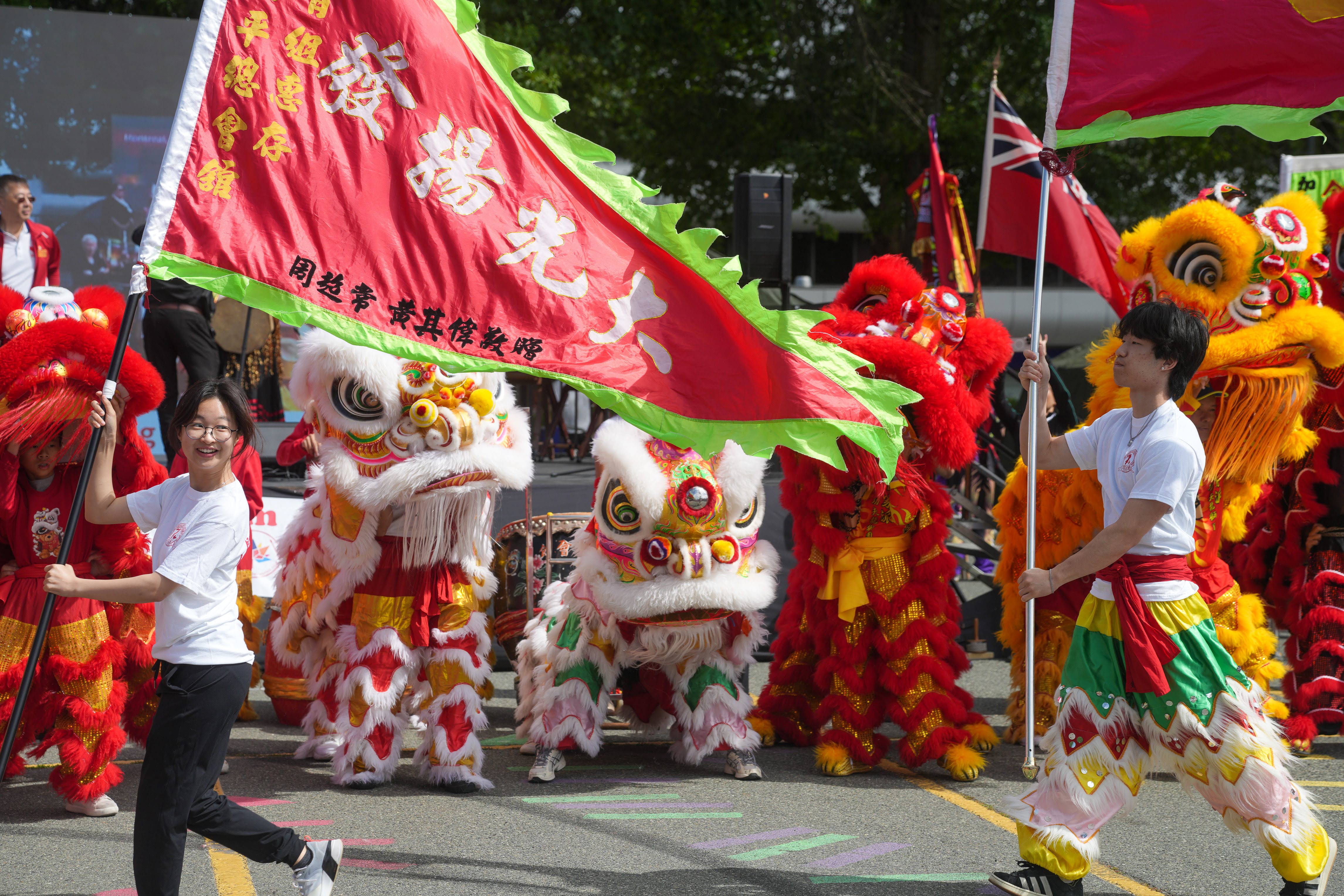 Lion dance performers on stage at an outdoor festival with a large crowd watching